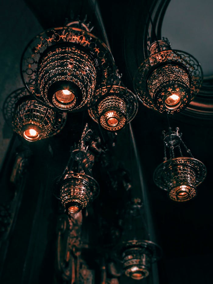 journey Low angle view of illuminated ornate metal chandeliers with intricate patterns in a dimly lit interior.