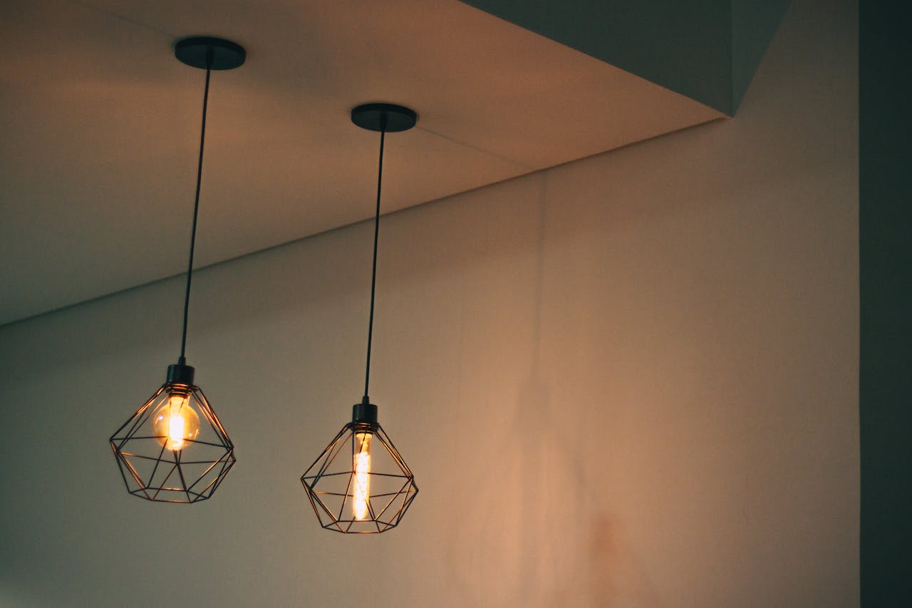 Stylish geometric pendant light fixtures casting warm light in a minimalistic indoor setting.